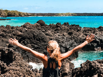 Woman standing on rock by sea against sky