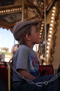 Cute boy sitting in carousel at amusement park