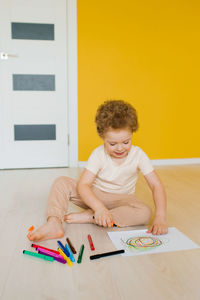 Cute little boy is sitting at home on the floor and drawing a drawing with colored pencil