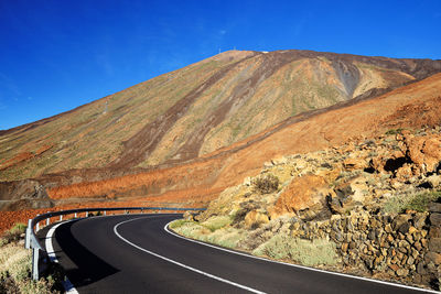 Empty road along rocky landscape against blue sky