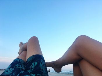 Low section of woman relaxing against blue sky