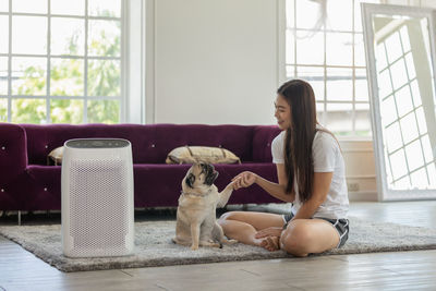 Full length of woman holding paw of dog sitting at home