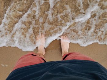 Low section of man standing by surf reaching on shore