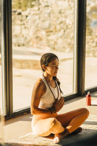 Female coach with eyes closed practicing prayer pose sitting cross-legged at retreat center