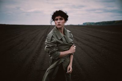 Portrait of young woman standing on field against sky