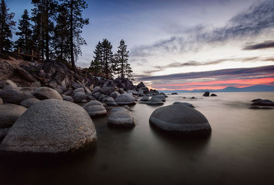 Rocks by sea against sky during sunset