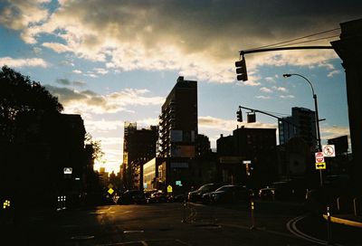 City street by buildings against sky during sunset