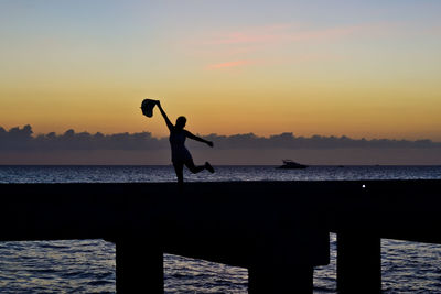 Silhouette woman dancing on pier over sea against sky during sunset