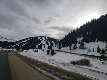 Snow covered road by trees against sky