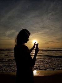 Side view of man drinking water at beach against sky during sunset