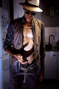 Midsection of man wearing hat standing against wall at home