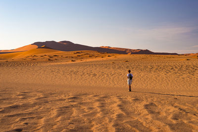 Man standing on sand dune in desert against sky