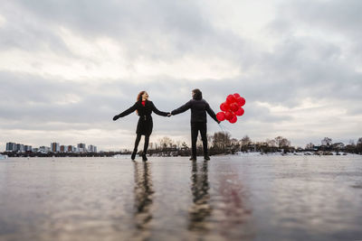 Rear view of couple holding hand standing on frozen lake against sky