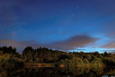 A starry sky in the clouds and a comet over a forest lake just after sunset..