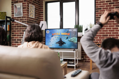 Rear view of woman using digital tablet while sitting on sofa at home