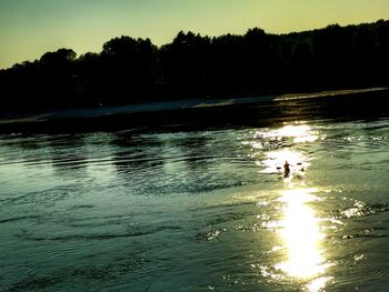 Silhouette swimming in lake against sky during sunset