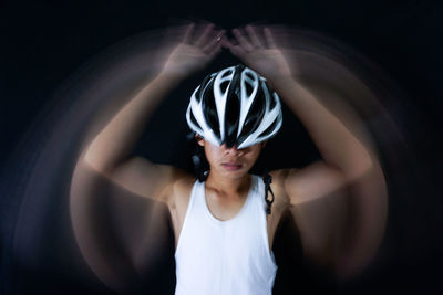 Close-up of man with blurred hands wearing bicycle helmet against black background