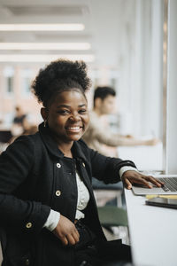 Portrait of smiling female student sitting with laptop at table in university