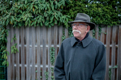 Portrait of man wearing hat standing against fence