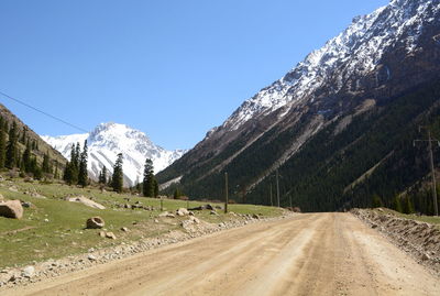 Road by snowcapped mountains against clear sky