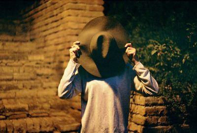 Person covering face with hat while standing outdoors