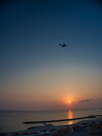 Airplane flying over sea against clear sky during sunset