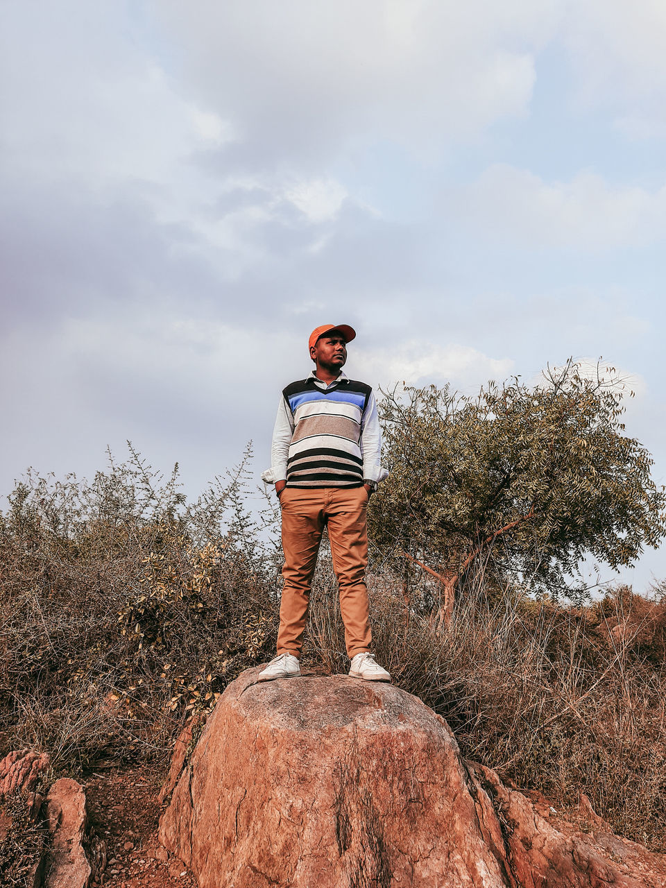 one person, sky, rock - object, rock, leisure activity, casual clothing, cloud - sky, plant, tree, solid, real people, standing, lifestyles, nature, full length, day, land, front view, young men, outdoors