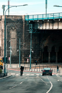 A city street with a car and biker under a bridge