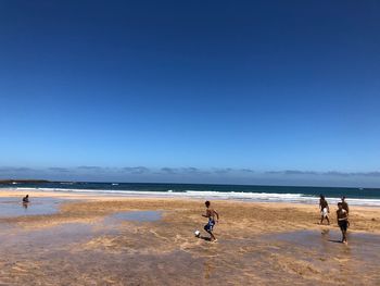 People on beach against clear blue sky