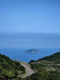 Scenic view of road by sea against blue sky
