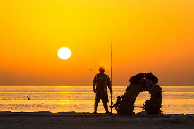 Friends standing on sea shore against sky during sunset