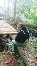 Side view of man sitting on sidewalk in forest