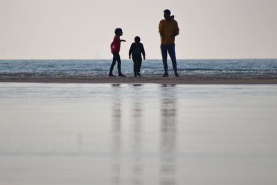 Men standing on beach against sky during sunset