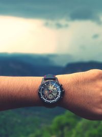 Close-up of hand holding clock against sky