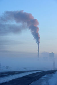 Smoke emitting from factory against sky during winter