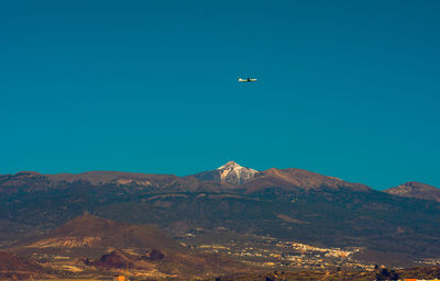 Airplane flying over mountains against clear blue sky