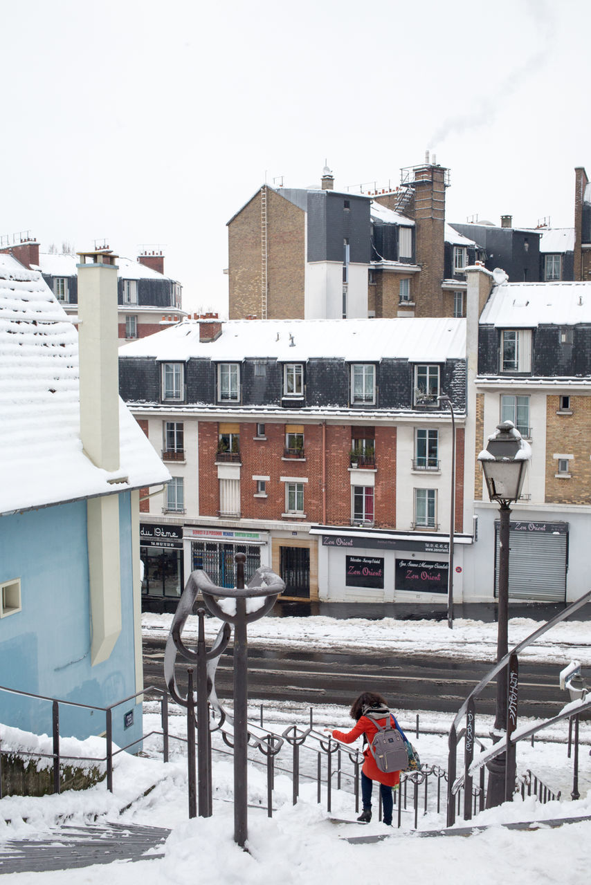 architecture, built structure, building exterior, winter, snow, day, residential building, outdoors, cold temperature, one person, real people, full length, clear sky, city, warm clothing, nature, people