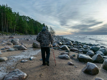 Rear view of man standing on rock at beach against sky