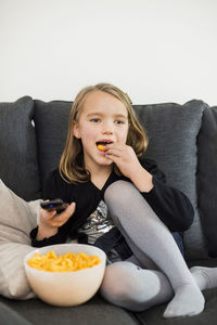 Girl eating snacks while watching tv on sofa at home
