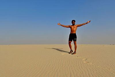 Full length of man standing on sand at beach against clear sky