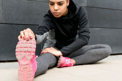 Young woman exercising while sitting on footpath