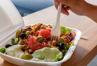 Female hand holing plastic fork, eating salad with fresh vegetables from take-out container