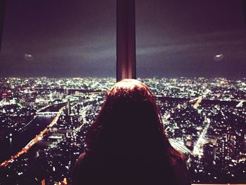 Rear view of woman against cityscape at night