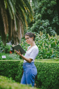 Young woman using phone while standing on plants