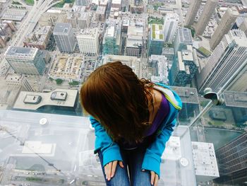 High angle view of woman sitting at window looking at cityscape