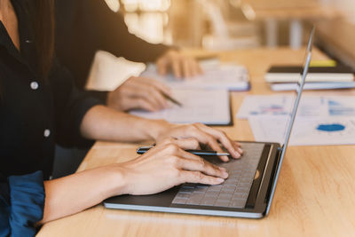 Midsection of woman using smart phone while sitting on table