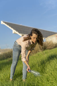 Woman on a meadow picking up empty plastic bottle