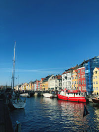 Boats in canal at harbor against clear blue sky