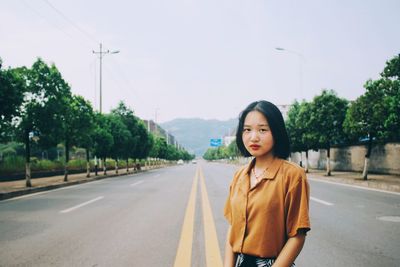 Portrait of young woman standing on road against trees