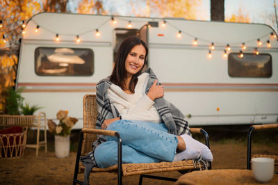 Portrait of smiling woman sitting on chair against camper van